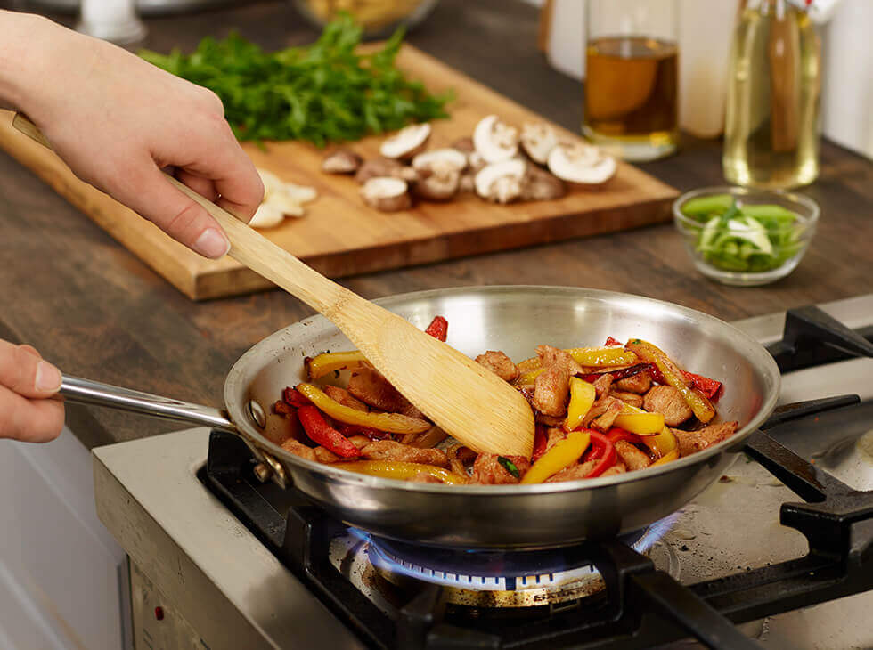 Sauteing chicken and vegetables in a skillet over a flame on kitchen stove
