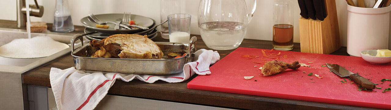 chicken in metal baking pan on kitchen counter next to red cutting board with carved pieces and knife
