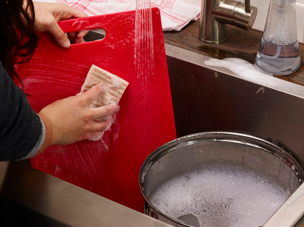 Person washing a red cutting board in the sink
