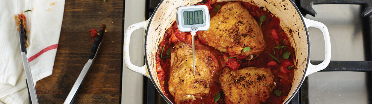 chicken thighs braising in a Dutch oven with vegetables and herbs with a digital thermometer reading 180 degrees