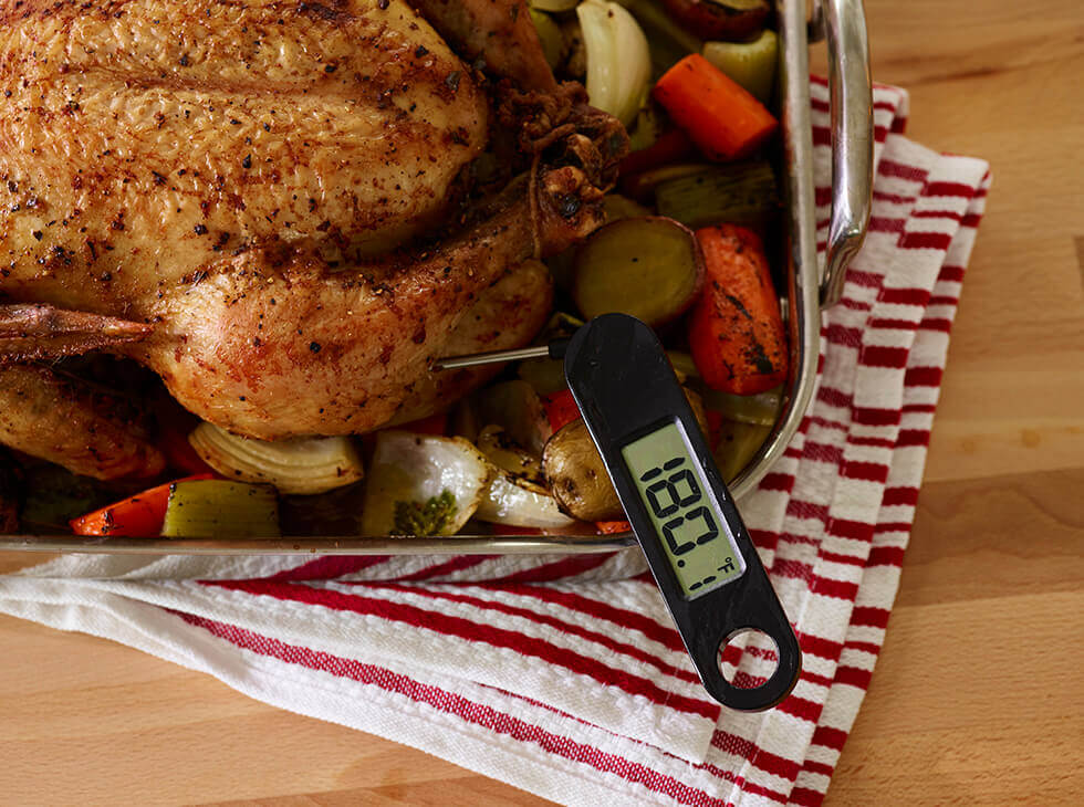 Whole roasted chicken with vegetables in a roasting pan with a digital thermometer reading 180